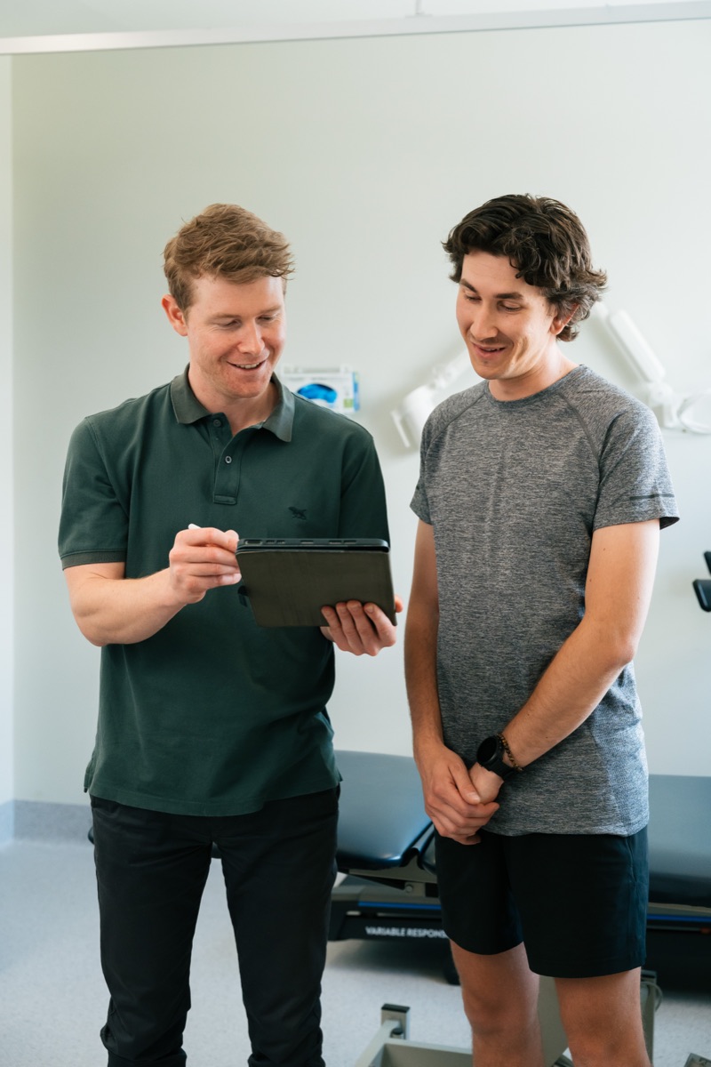 A physiotherapist recording assessment findings on a tablet with a client